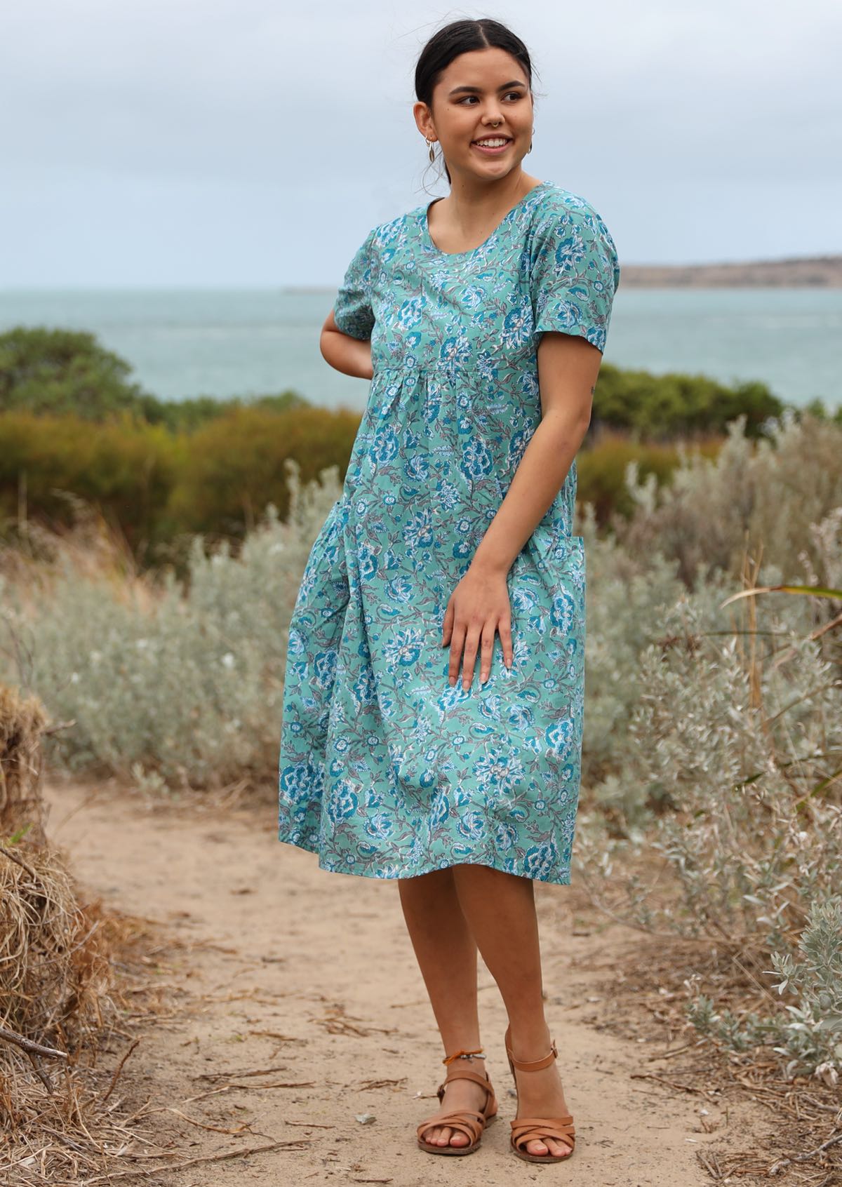 Model wearing over the knee length cotton dress with round neckline, short sleeves and empire waist.