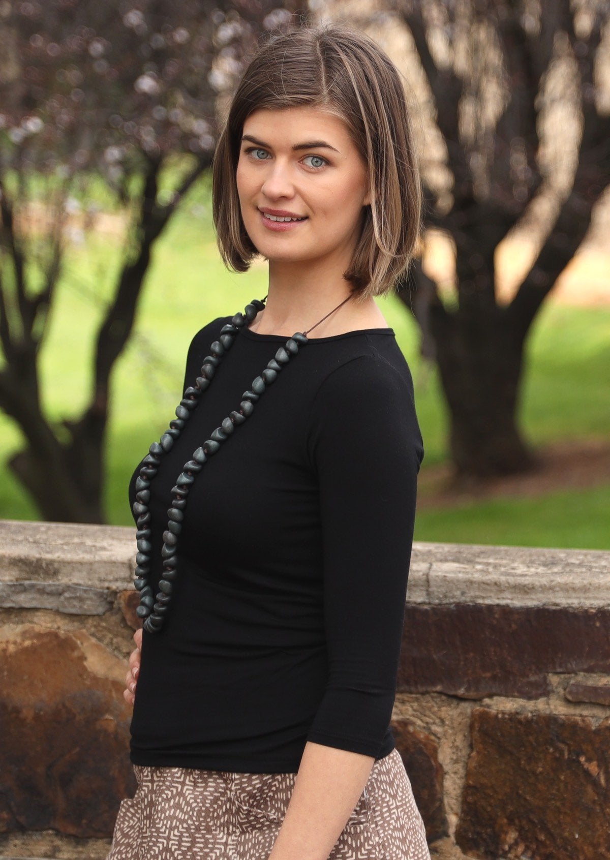 Woman wearing a rayon boat neck black 3/4 sleeve top with a grey beaded necklace.