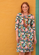 Model wears cotton dress with wide rounded neckline, 3/4 sleeve, knee length and pockets in pastel print
