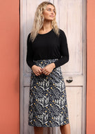 Model wears midi length cotton A-line skirt with wattle print on very dark blue base