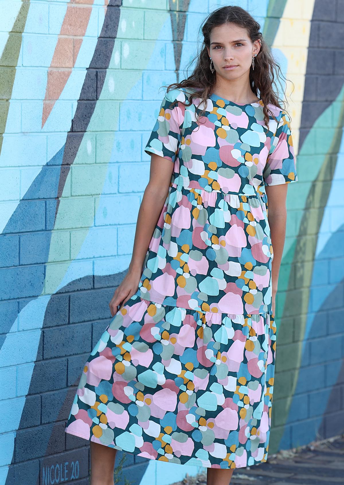 Model wearing Claudia Dress short sleeve high round neck, tiered loose fit cotton teal background with pastel coloured spots