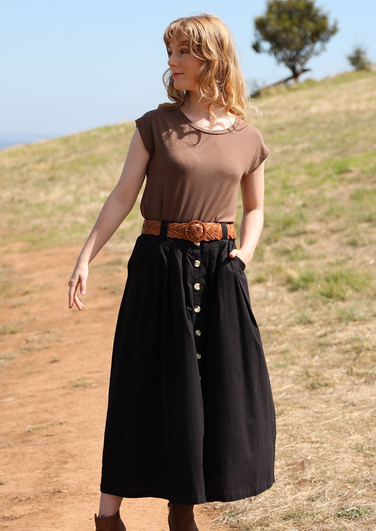 Woman wears 100% cotton midi length skirt with belt worn through belt loops, and hand in pocket