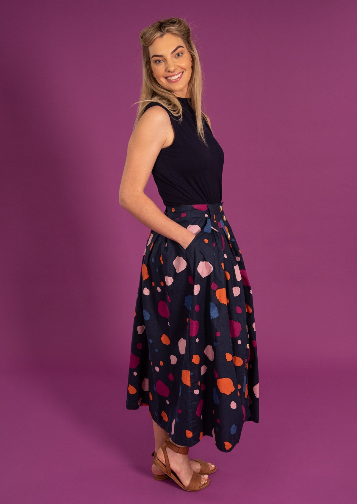 Woman stands sideways in midi length navy cotton skirt with colorful spotty print 
