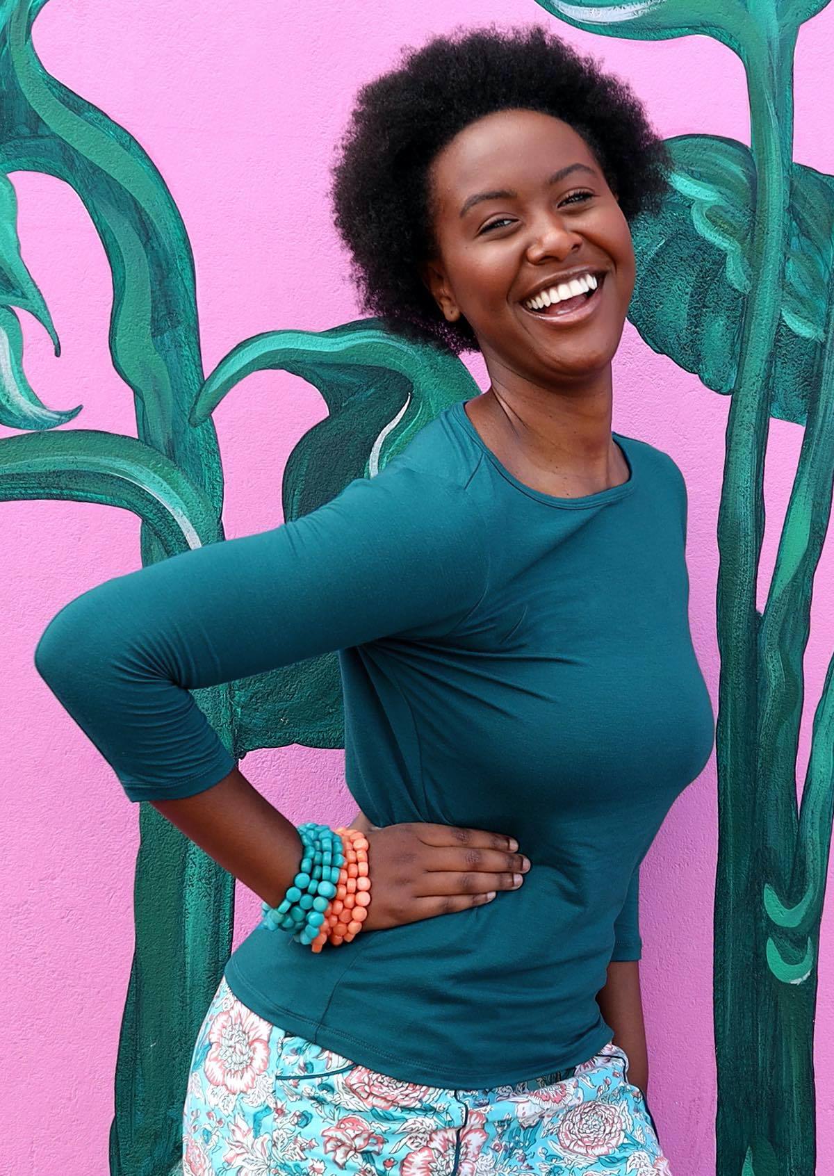Woman wearing a rayon boat neck teal 3/4 sleeve top with a floral blue skirt.