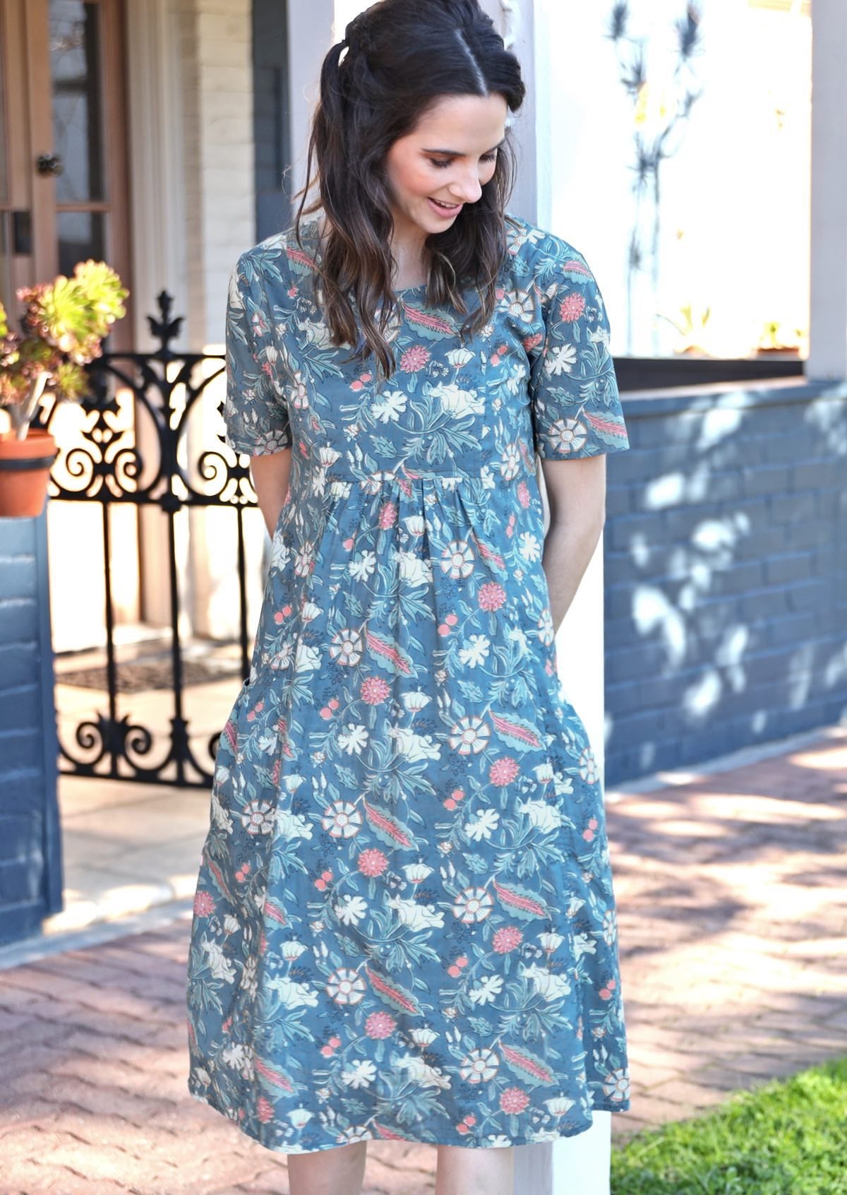 Woman leans on post wearing cotton relaxed fit floral print sun dress with short sleeves