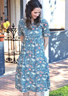 Woman leans on post wearing cotton relaxed fit floral print sun dress with short sleeves