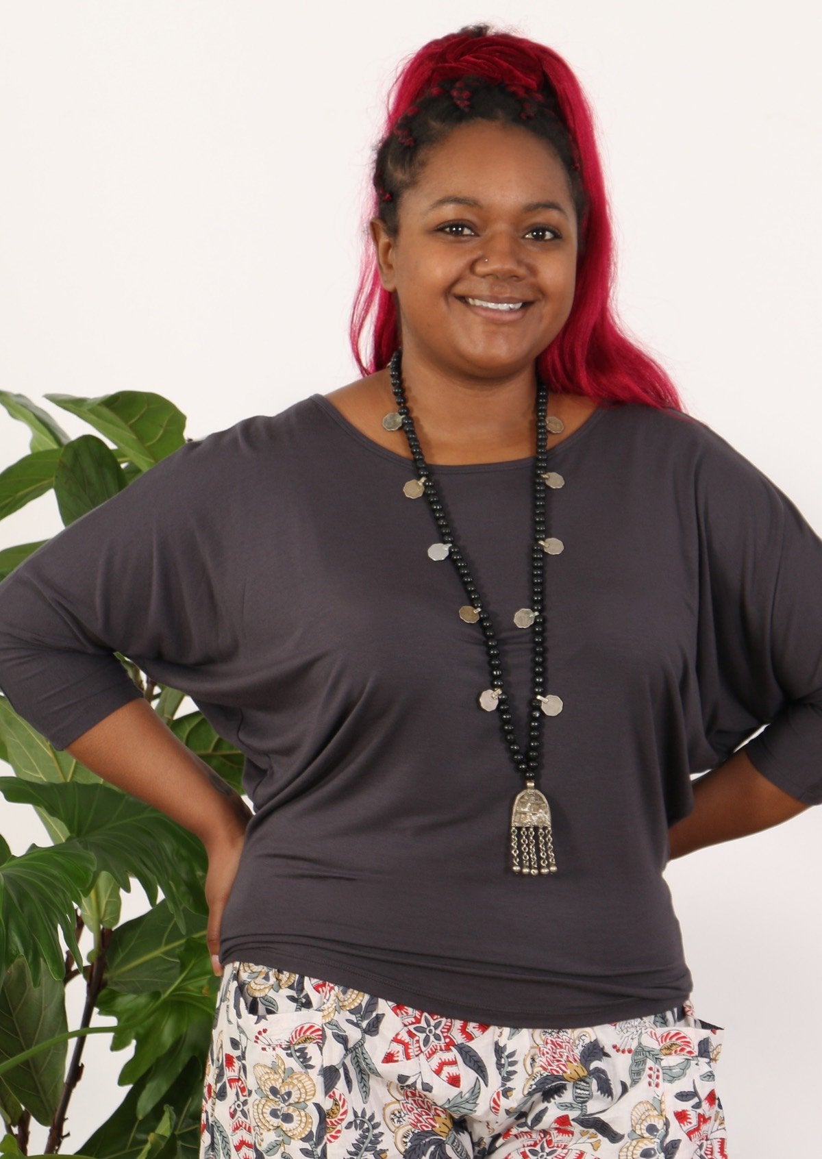 Woman wearing a 3/4 sleeve rayon batwing round neckline dark grey top with beaded necklace.