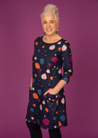 Model standing with hands in pockets wearing 100% cotton dress in bold and colourful printed dress.