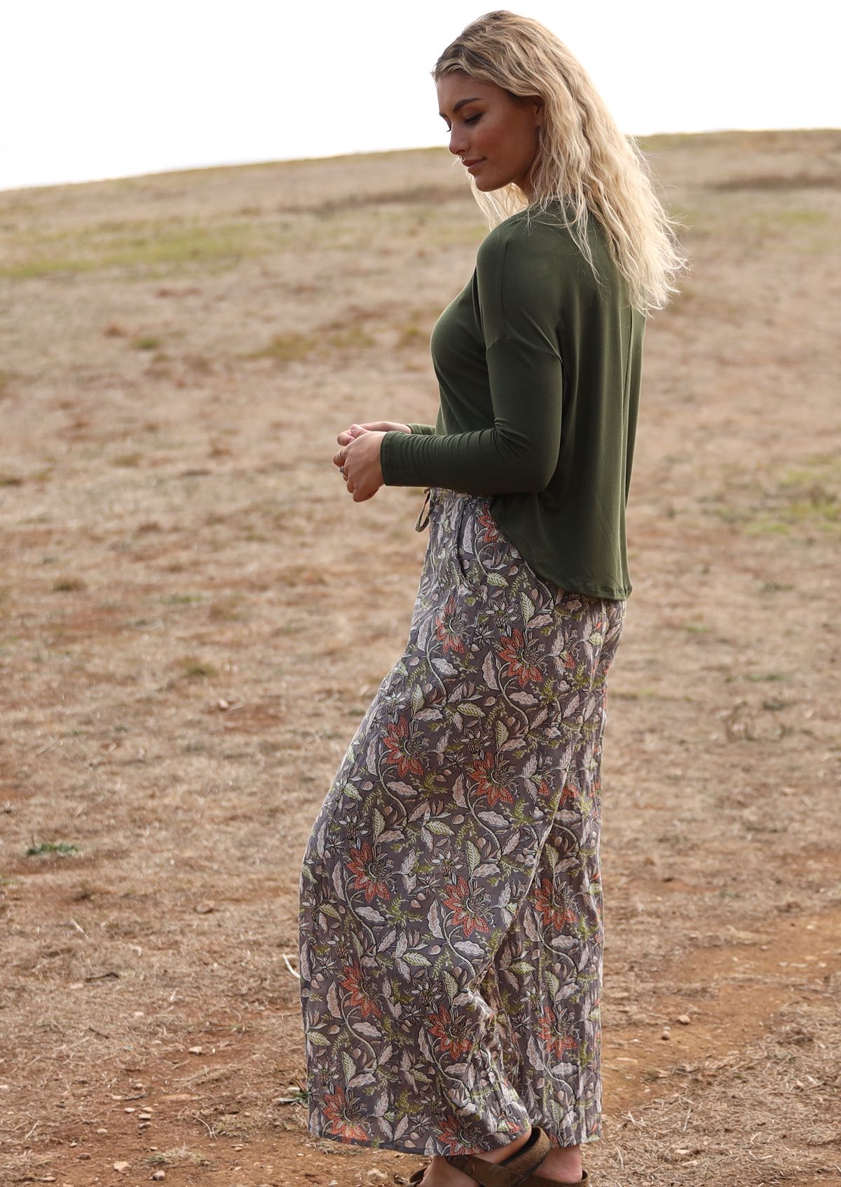 Woman stands side on in cotton wide leg pants with taupe based floral print, with drawstring and pockets