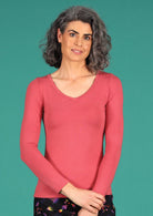Woman wearing a rose pink long sleeve stretch v-neck soft rayon top in front of green wall.