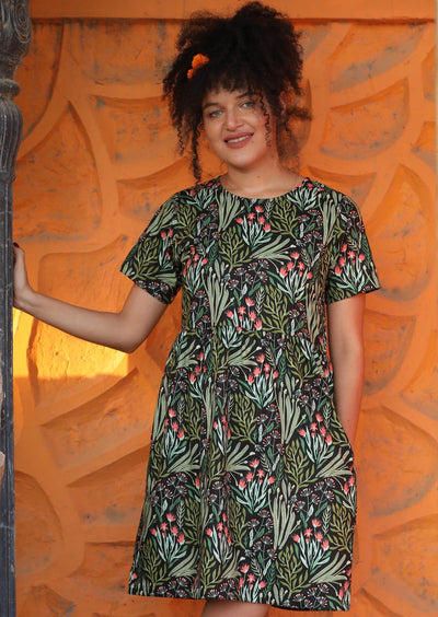 Model in Short Sleeve Relaxed fit Green Floral Cotton Dress with gathered pleats at waistline above knee length with pockets