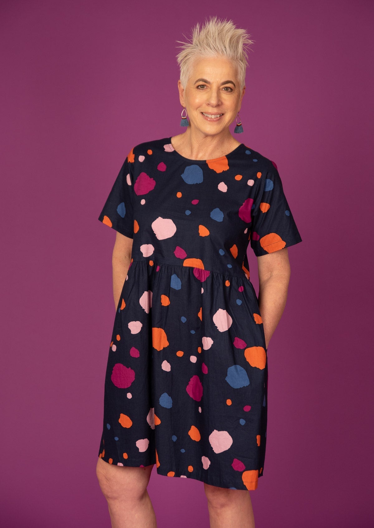 Woman wears 100% cotton loose fit dress with round neckline and short sleeves in colorful splotchy print on dark navy background.
