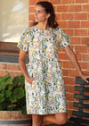 Woman in Mabel Dress Short Sleeve Relaxed fit light toned floral printed Cotton Dress cotton dress gathered pleats at waistline above knee length with pockets