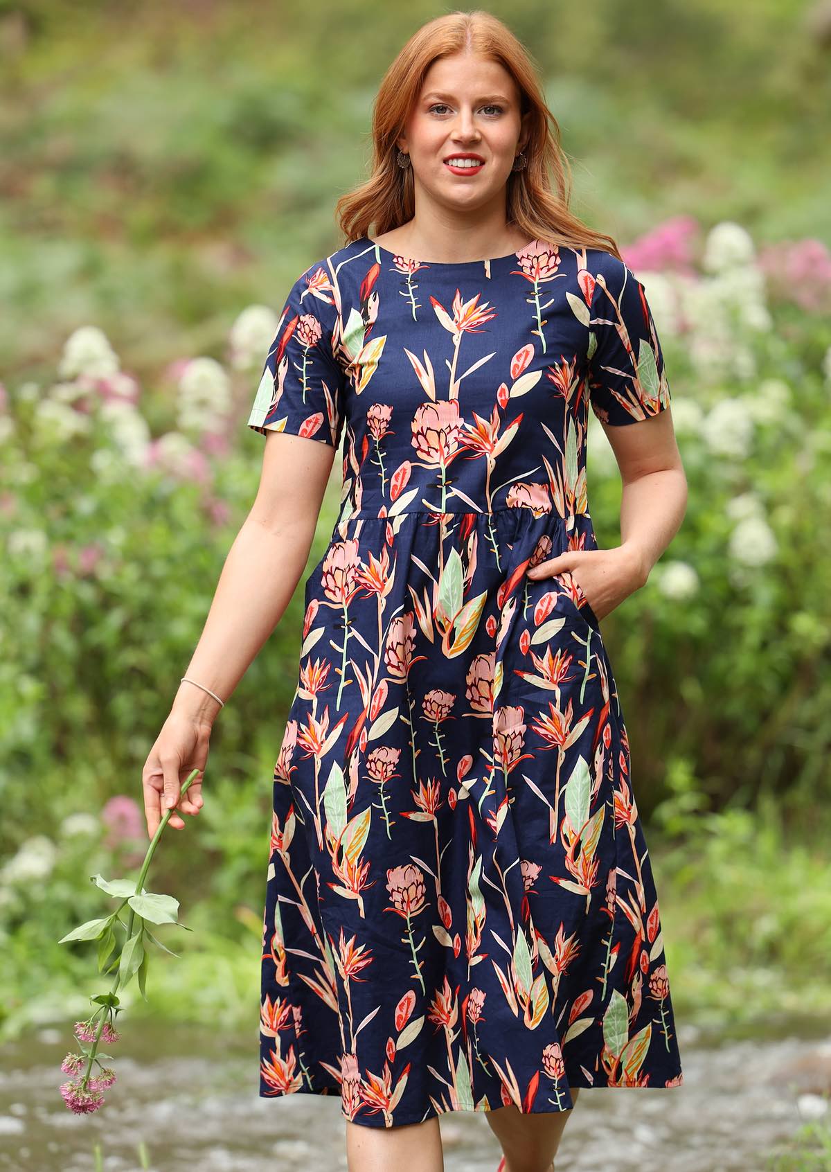 Woman wearing navy background pink and green toned native floral print midi dress with round neckline and  short sleeve 