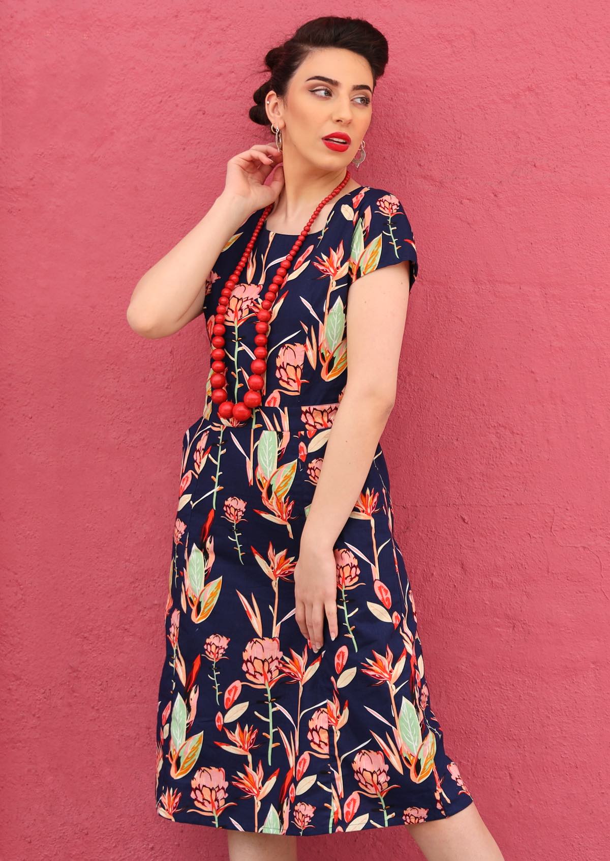 Model poses in cotton slight A-line dress with cap sleeves, paired with a chunky red beaded necklace