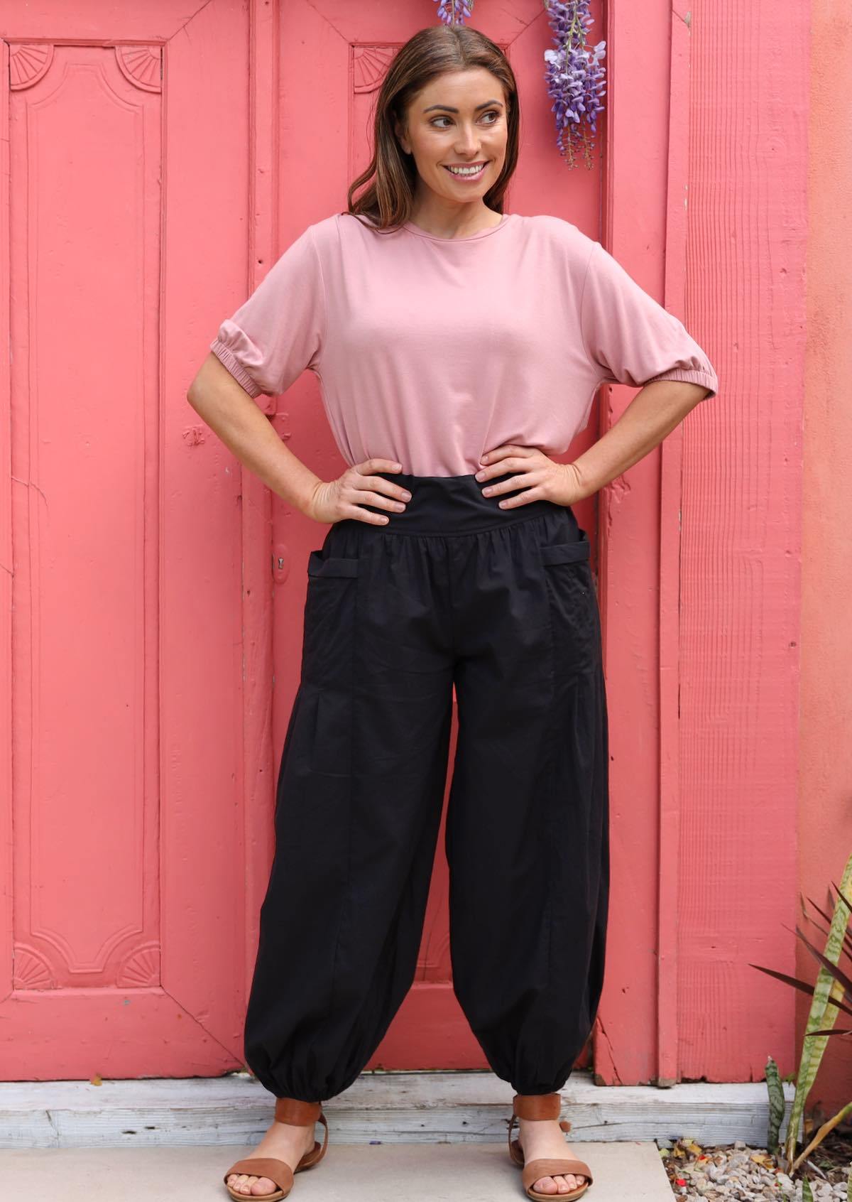 Woman poses in black elasticated ankle women's cotton pants with hands on waist