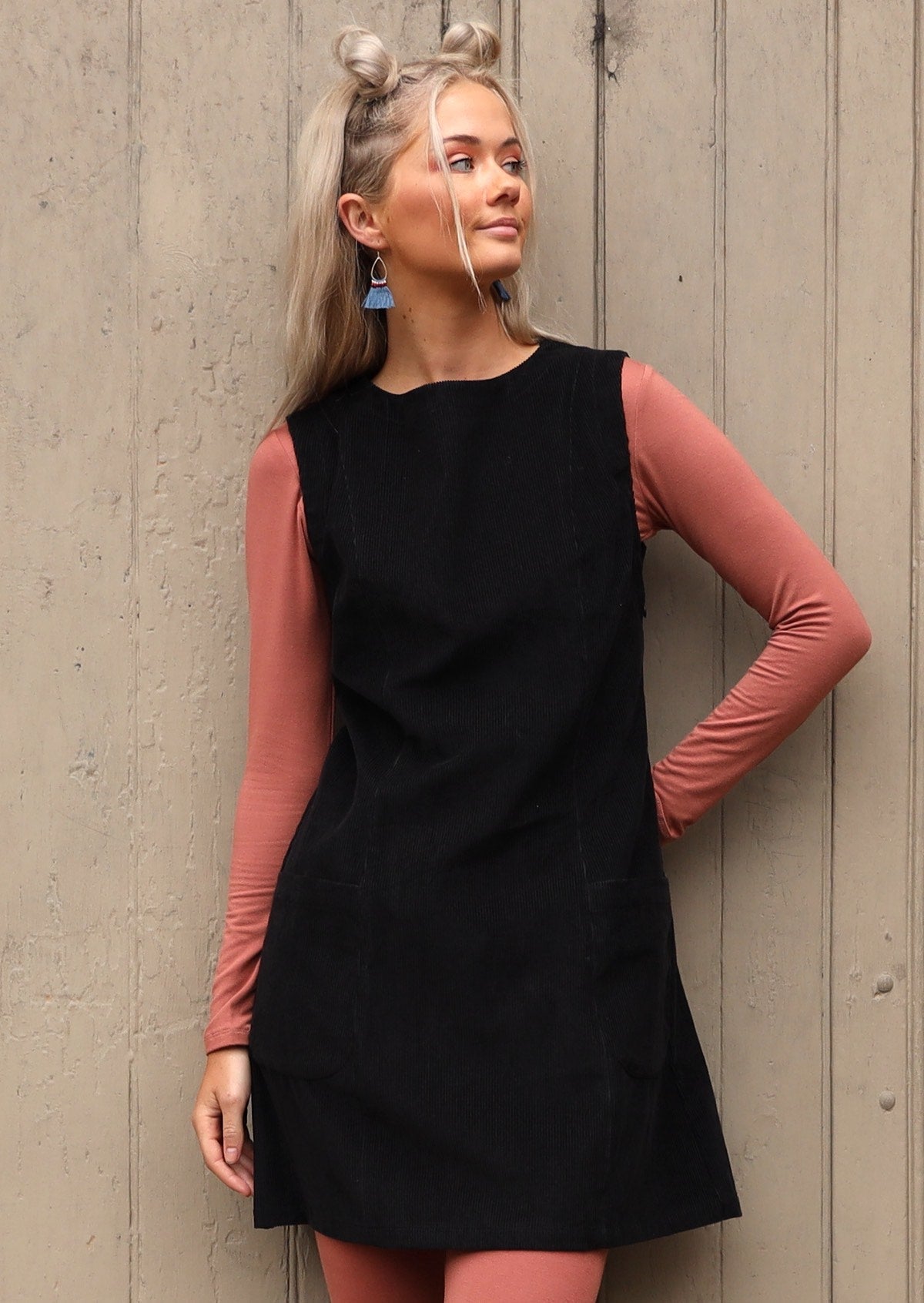 Woman poses in boat neck cotton corduroy sleeveless tunic dress with dusty pink top and leggings underneath