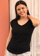 Front view of woman wearing a black v-neck short cap sleeve rayon top with cream pants