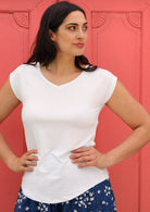 Woman wearing a white v-neck short cap sleeve rayon top in front of pink wall.