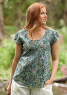 Woman wears 100% cotton cap sleeve top with pin tuck detail across the bust and a scoop neckline