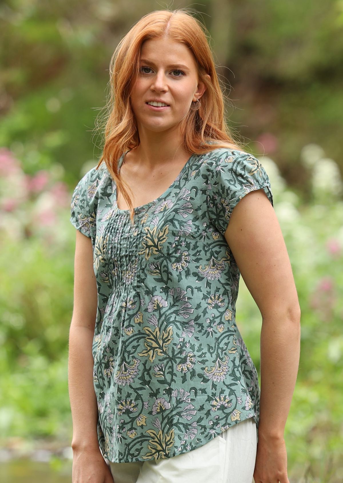 Woman wears cotton short sleeve top with scoop round neckline and pleated detail across the bodice